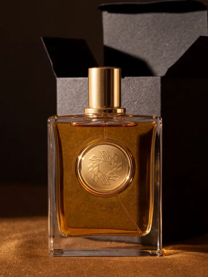 An amber perfume bottle with a gold medallion, held and sprayed